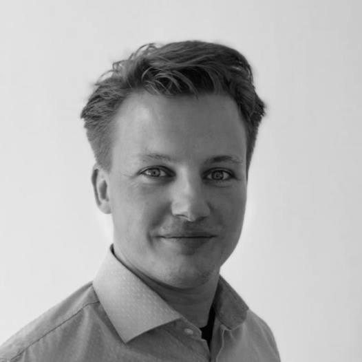 Portret van een man met kort golvend haar, glimlachend en gekleed in een licht overhemd tegen een witte achtergrond.