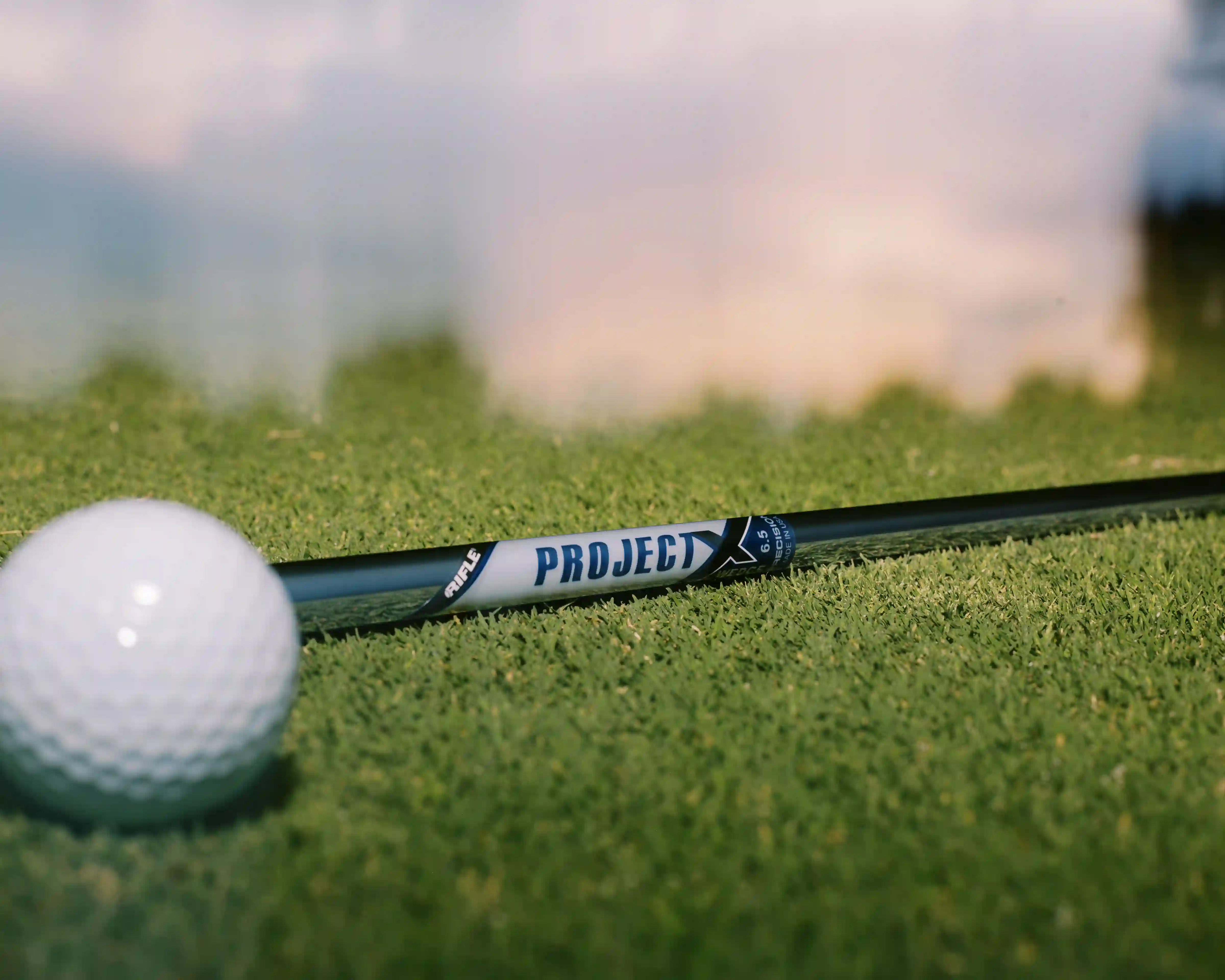 Close-up of a golf ball and a Project X golf club shaft lying on green grass.