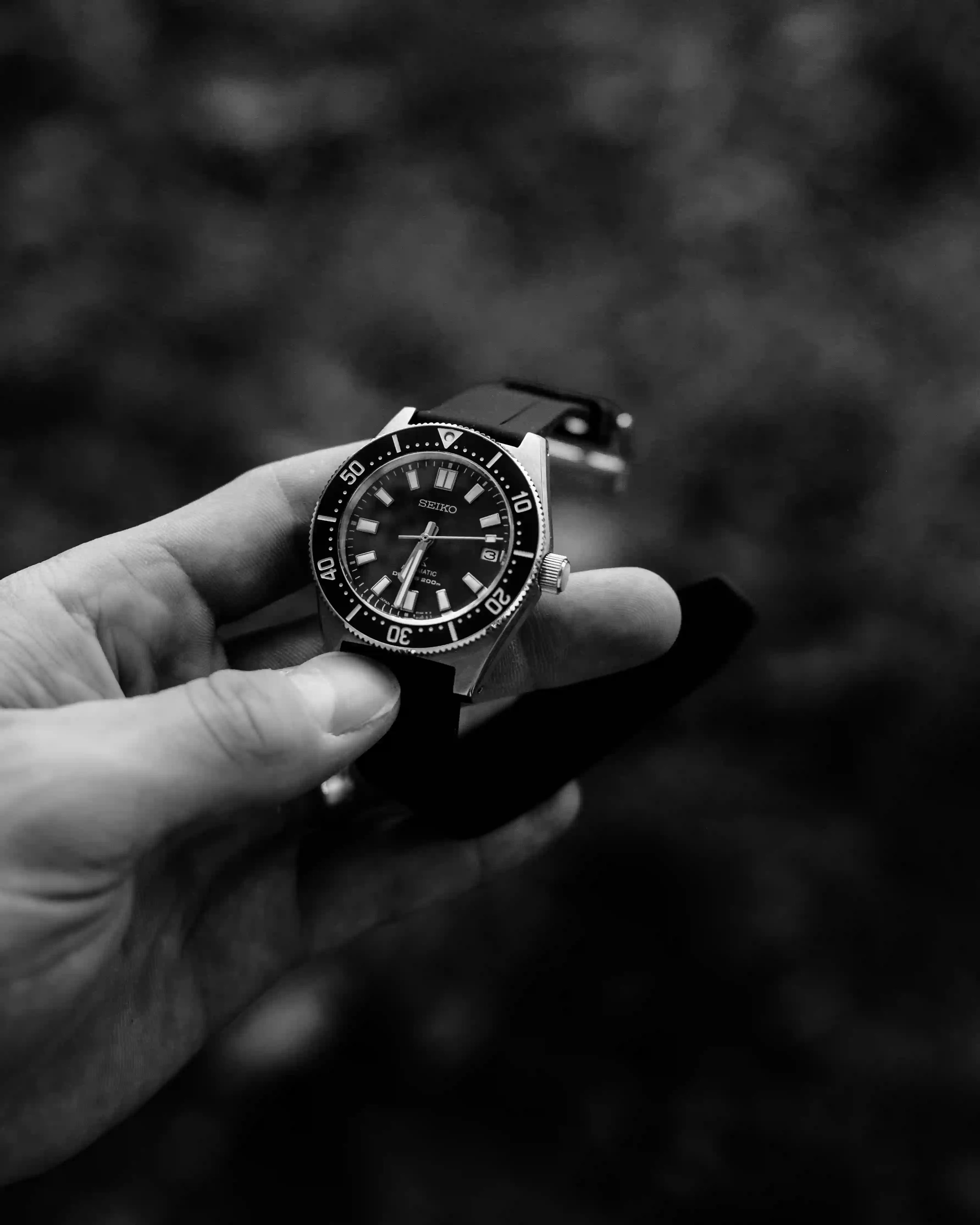 Hand holding a Seiko diver watch with a black bezel and strap, showing the time at approximately 6:33.