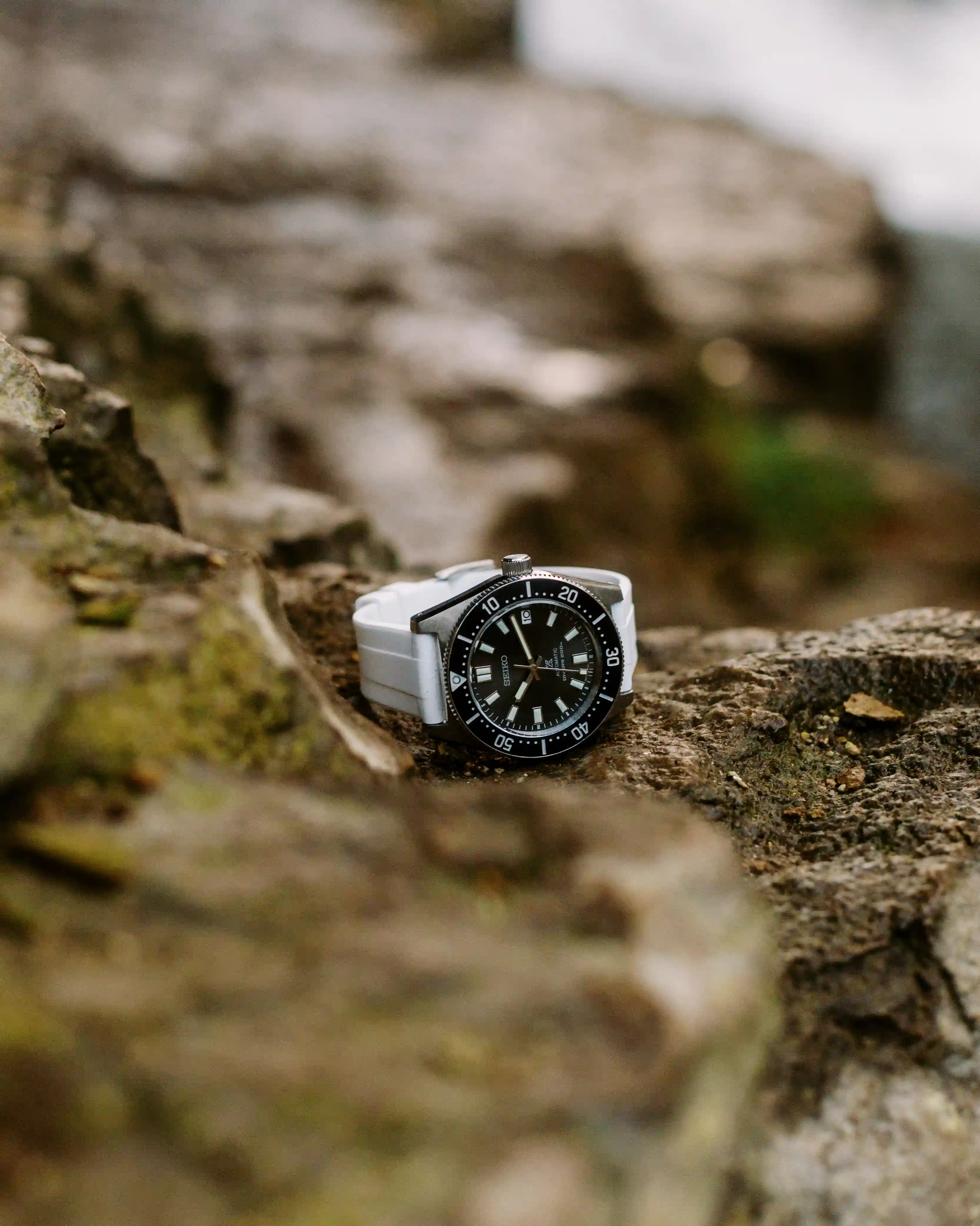 Seiko dive watch with a black dial and white strap resting on a rough outdoor rock surface.