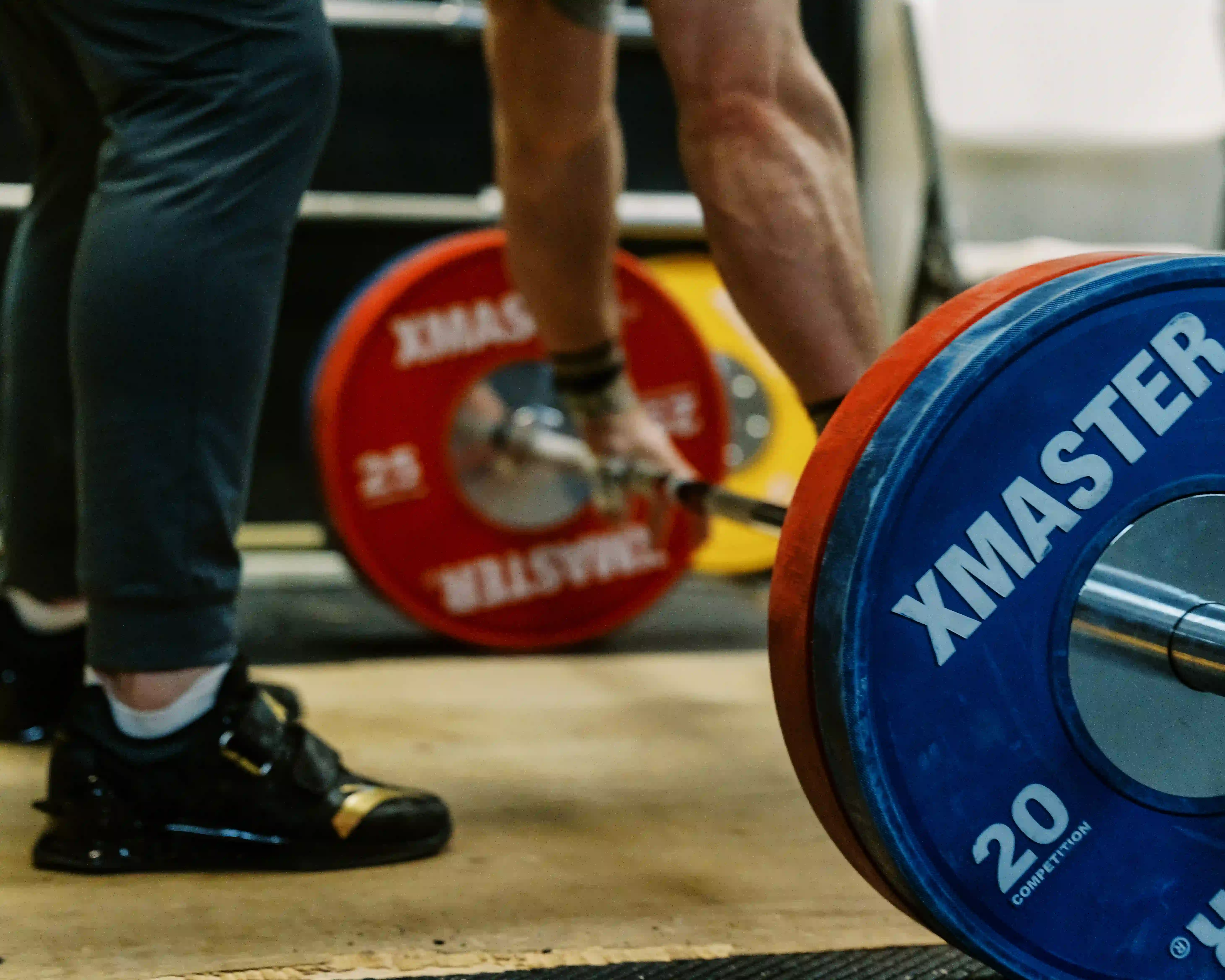 Close-up of a weightlifter gripping a barbell loaded with colorful weight plates on a gym floor.