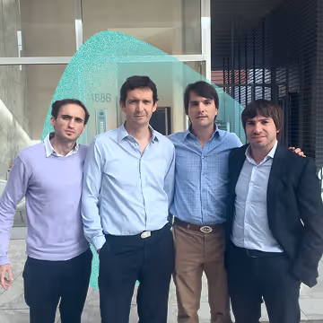 Four men standing together outdoors in front of a building, dressed in business casual and formal attire.