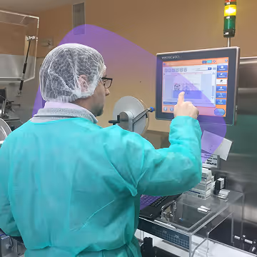 Person in protective medical attire operating a touchscreen in a sterile lab environment.