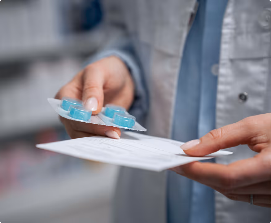 Person in a white coat holding a blister pack of blue pills and a prescription paper.