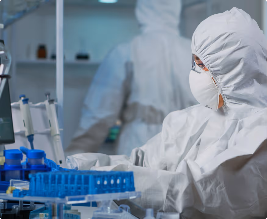 Scientist in full protective gear working at a laboratory bench with test tubes and scientific equipment.