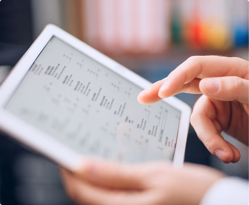 Close-up of a person's hand interacting with a tablet displaying text and data.