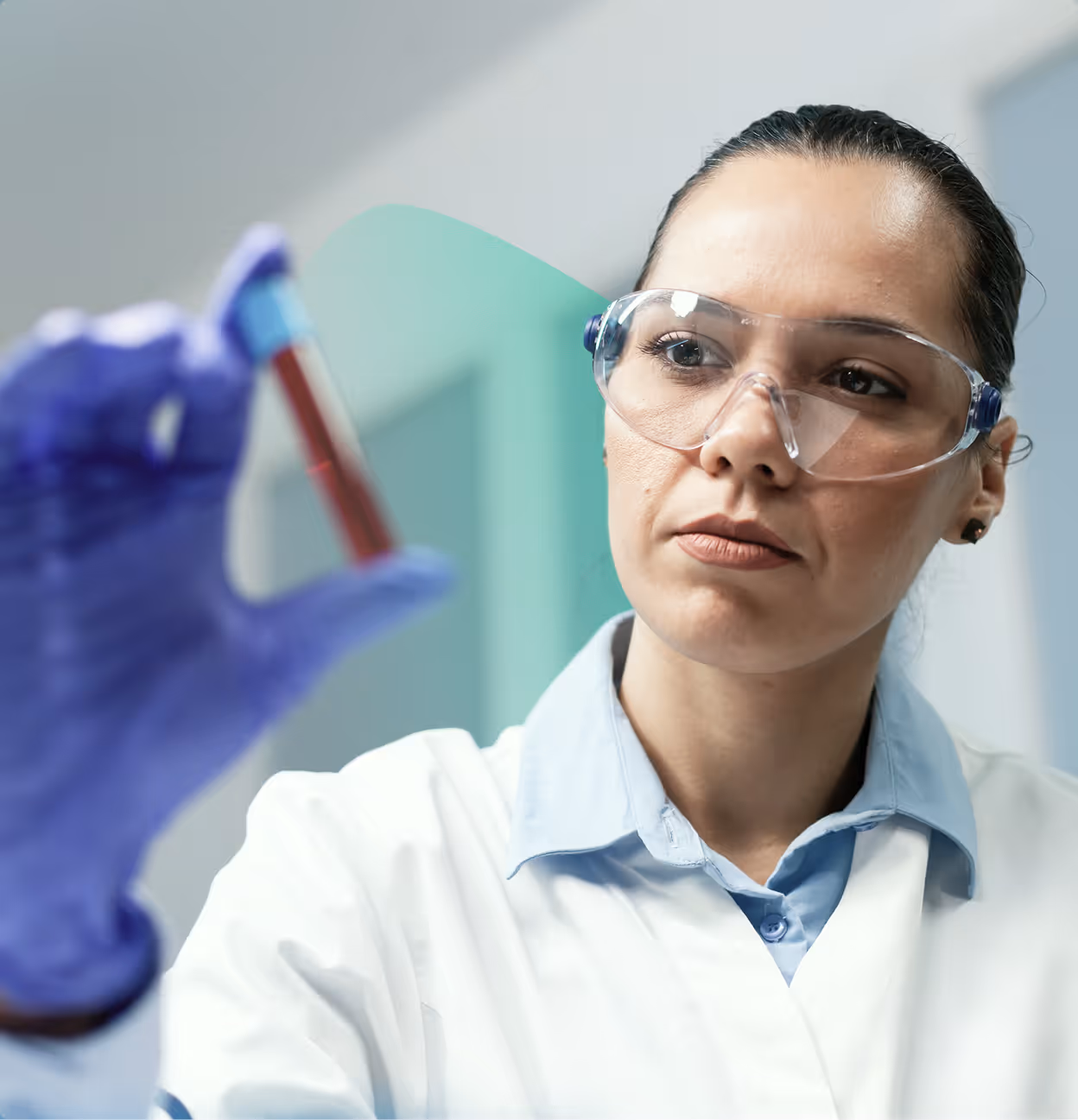 Female scientist in safety glasses and lab coat examining a test tube with red liquid in a laboratory.