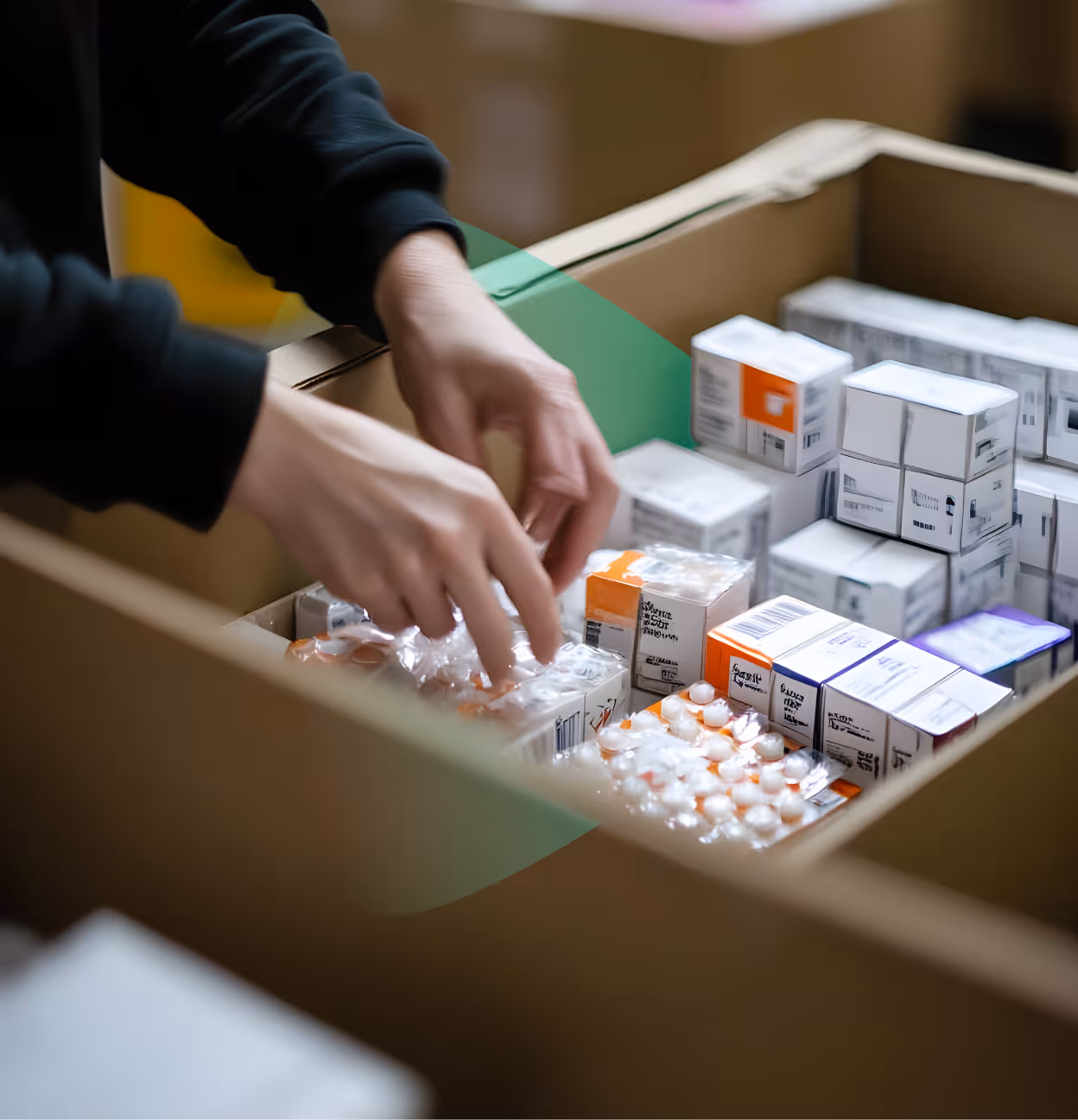 Hands organizing blister packs and boxes of medication inside a cardboard box.