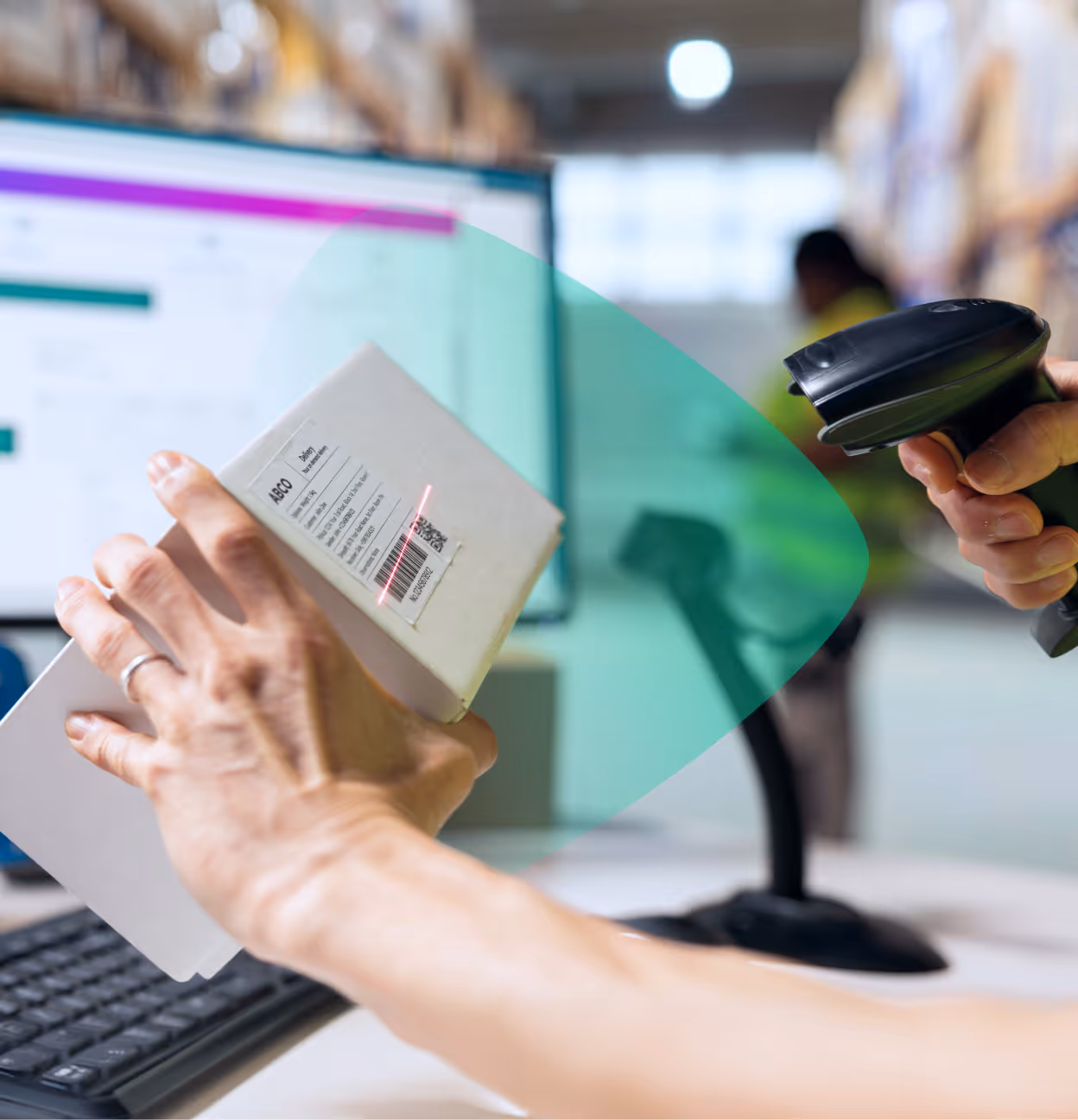 Hand holding a package being scanned by a barcode scanner in a warehouse or shipping area.