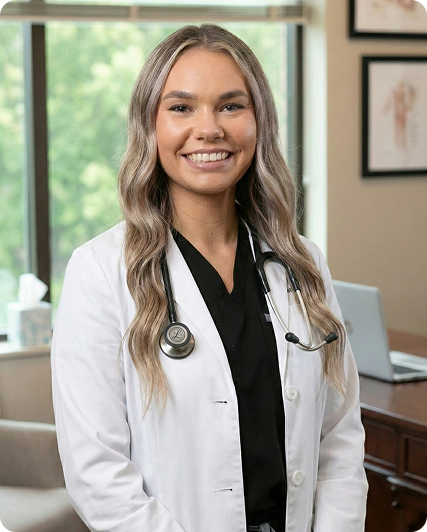 Female healthcare provider with a stethoscope smiling in a modern medical office, representing professional primary care and personalized patient services.