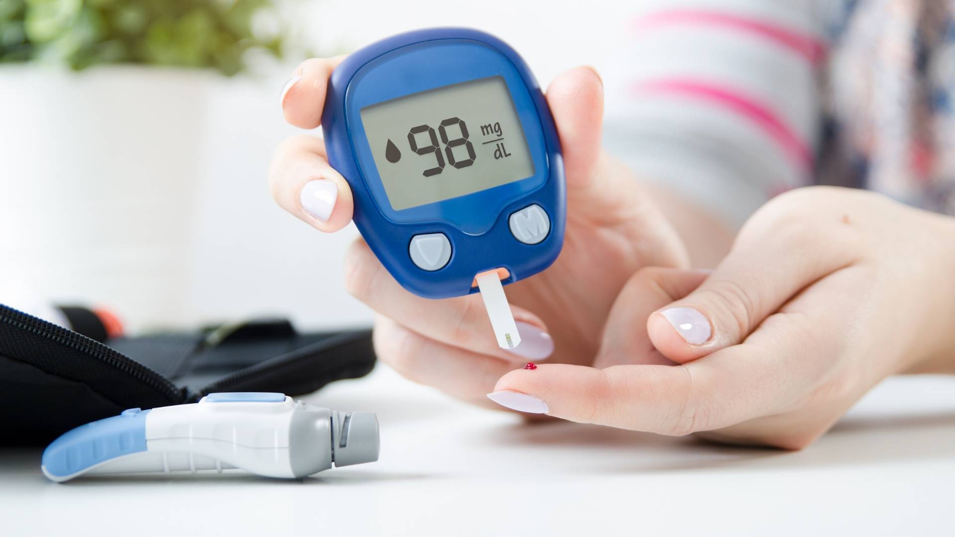 A person holding a blue digital glucose meter that displays a reading of 98 mg/dL after a blood sugar test.