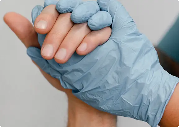 A hand wearing a blue medical glove gently holding a bare hand, symbolizing care or support.