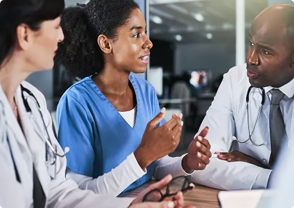 Three medical professionals having a discussion, with one nurse in blue scrubs explaining to two doctors.