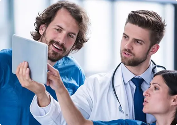 Two doctors and a healthcare professional reviewing information on a tablet in a clinical setting.