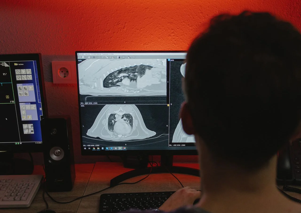 Person viewing CT scan images of lungs and heart on a computer monitor in a dimly lit room.