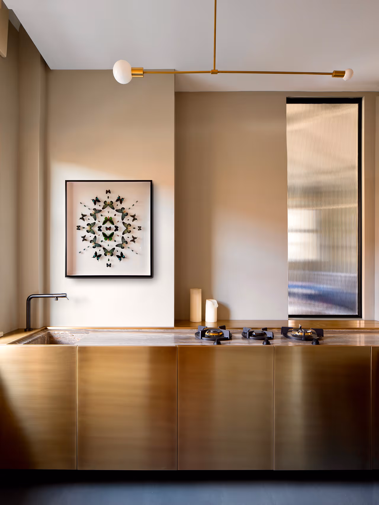 Modern kitchen with brass cabinets, built-in gas stove, black faucet, and framed butterfly artwork on beige wall.