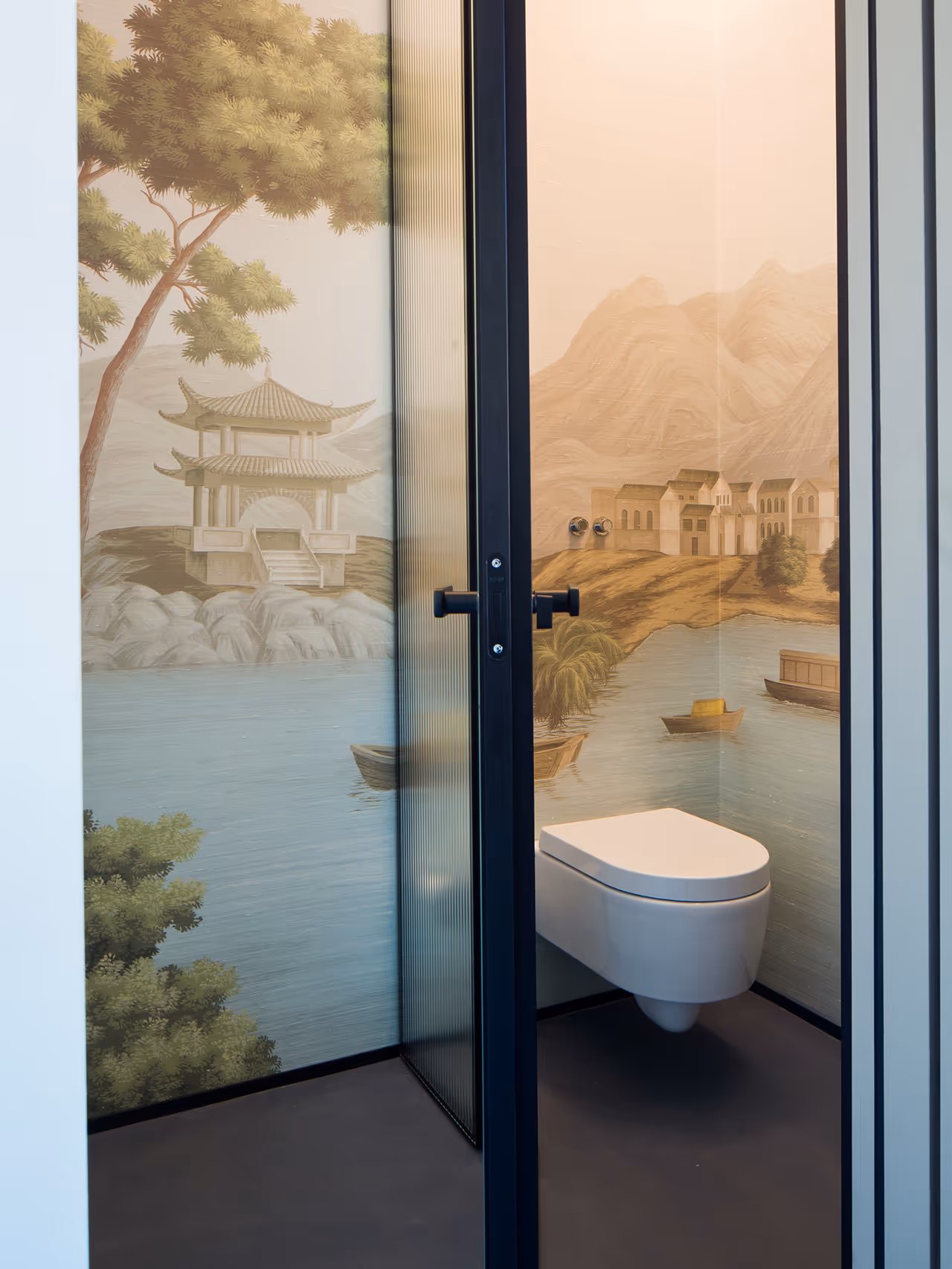 Modern bathroom with a wall-mounted toilet and mural depicting a serene lakeside scene with pagoda, boats, and mountains.