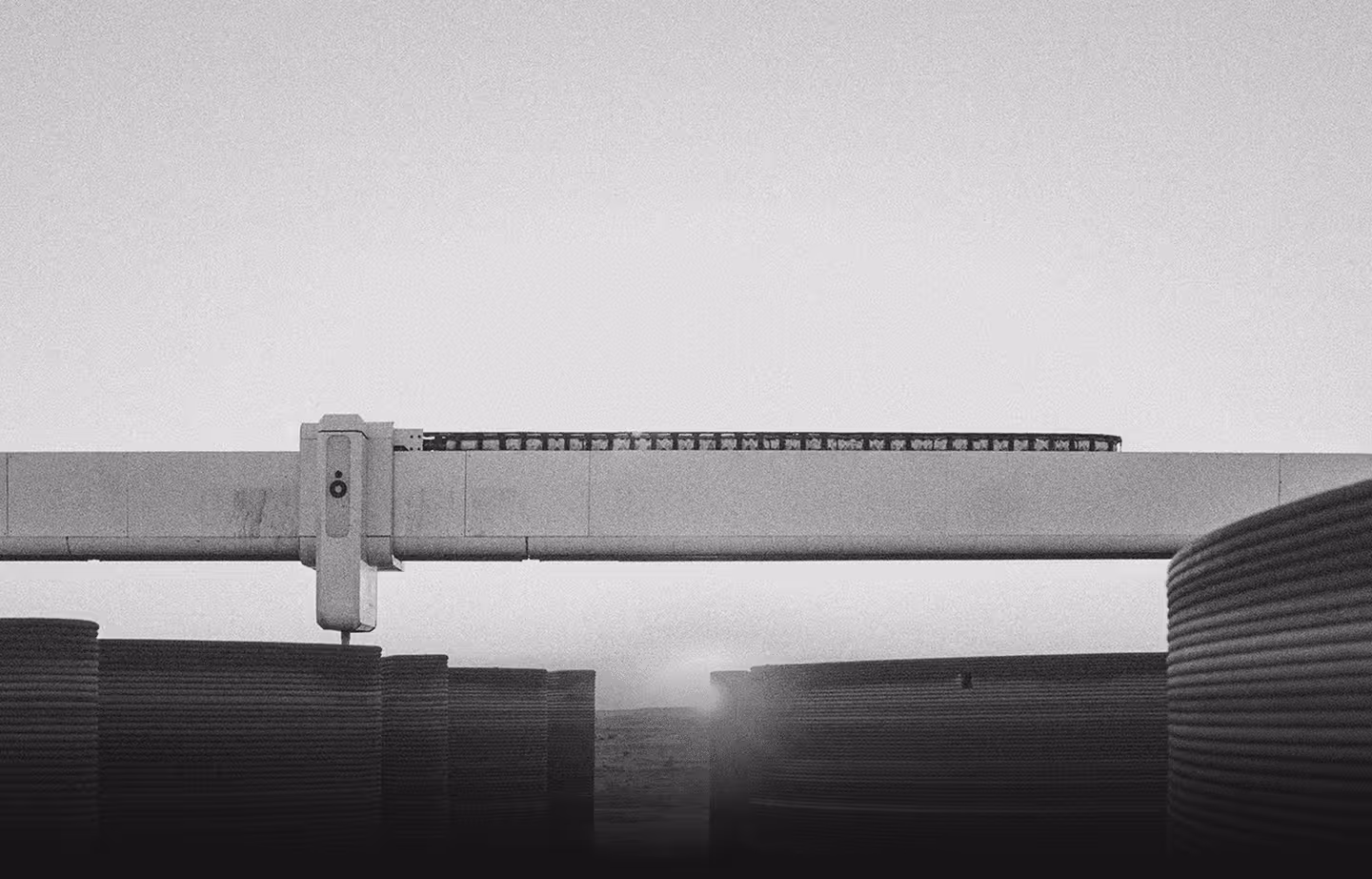Gantry 3D printer extruder spanning cylindrical printed concrete walls.