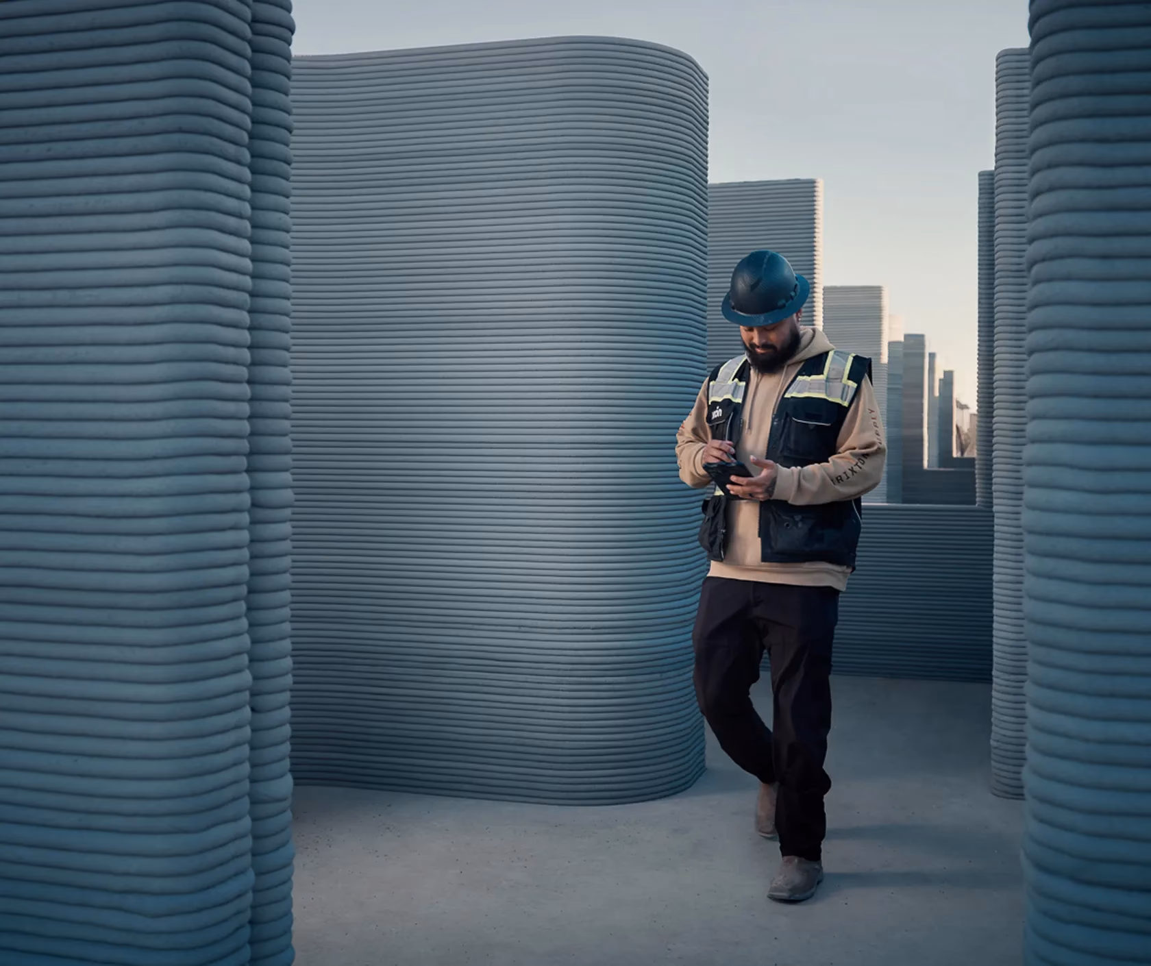 Construction worker in hard hat using tablet between 3D-printed layered concrete walls