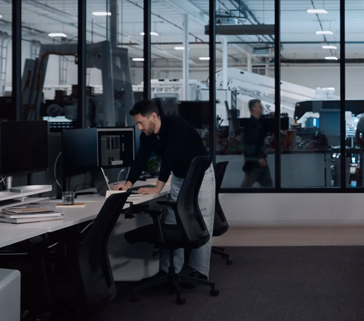 Engineer reviewing plans at desk overlooking robotic 3D-printing workshop and factory floor