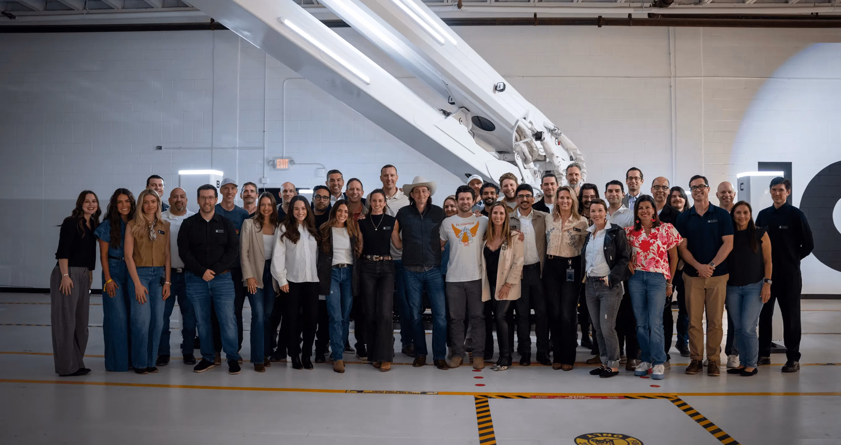Icon Build team posed in front of a large robotic 3D‑printing arm inside a fabrication/production facility