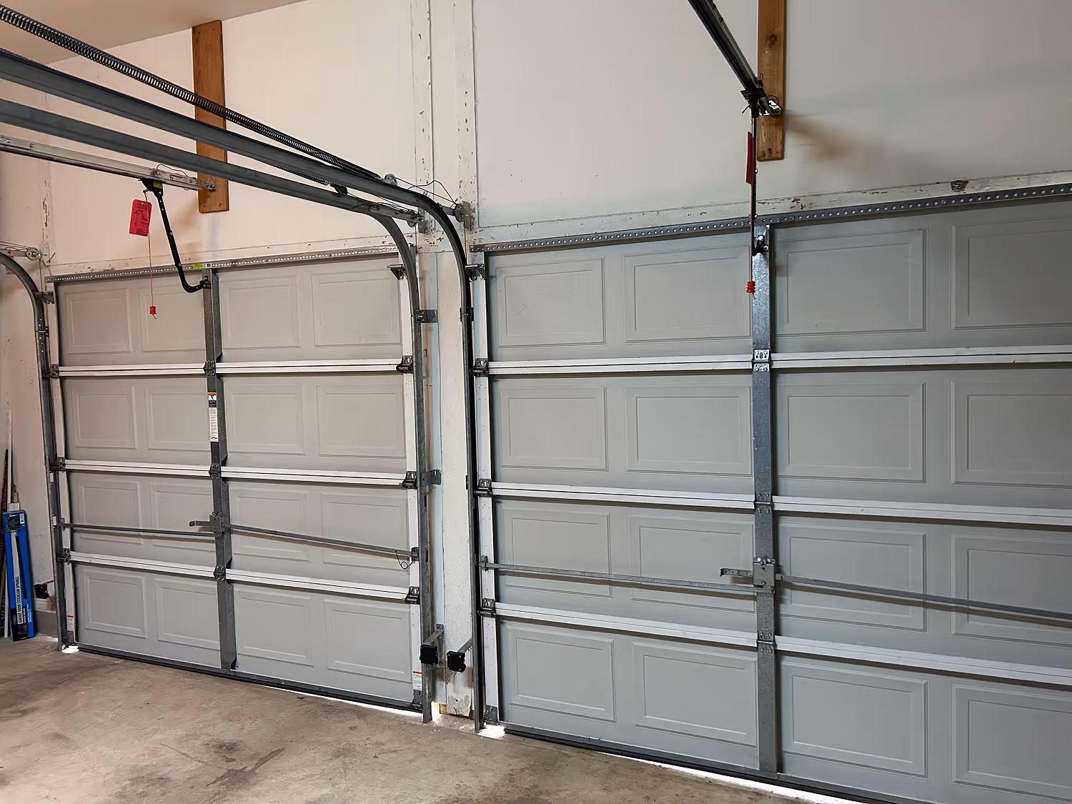 Two closed grey sectional garage doors inside a garage with concrete floor and white walls.