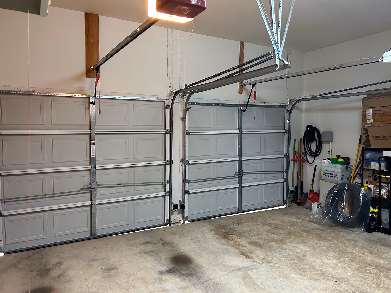 Clean, spacious two-car garage with closed light gray garage doors and various tools and boxes stored along the right wall.