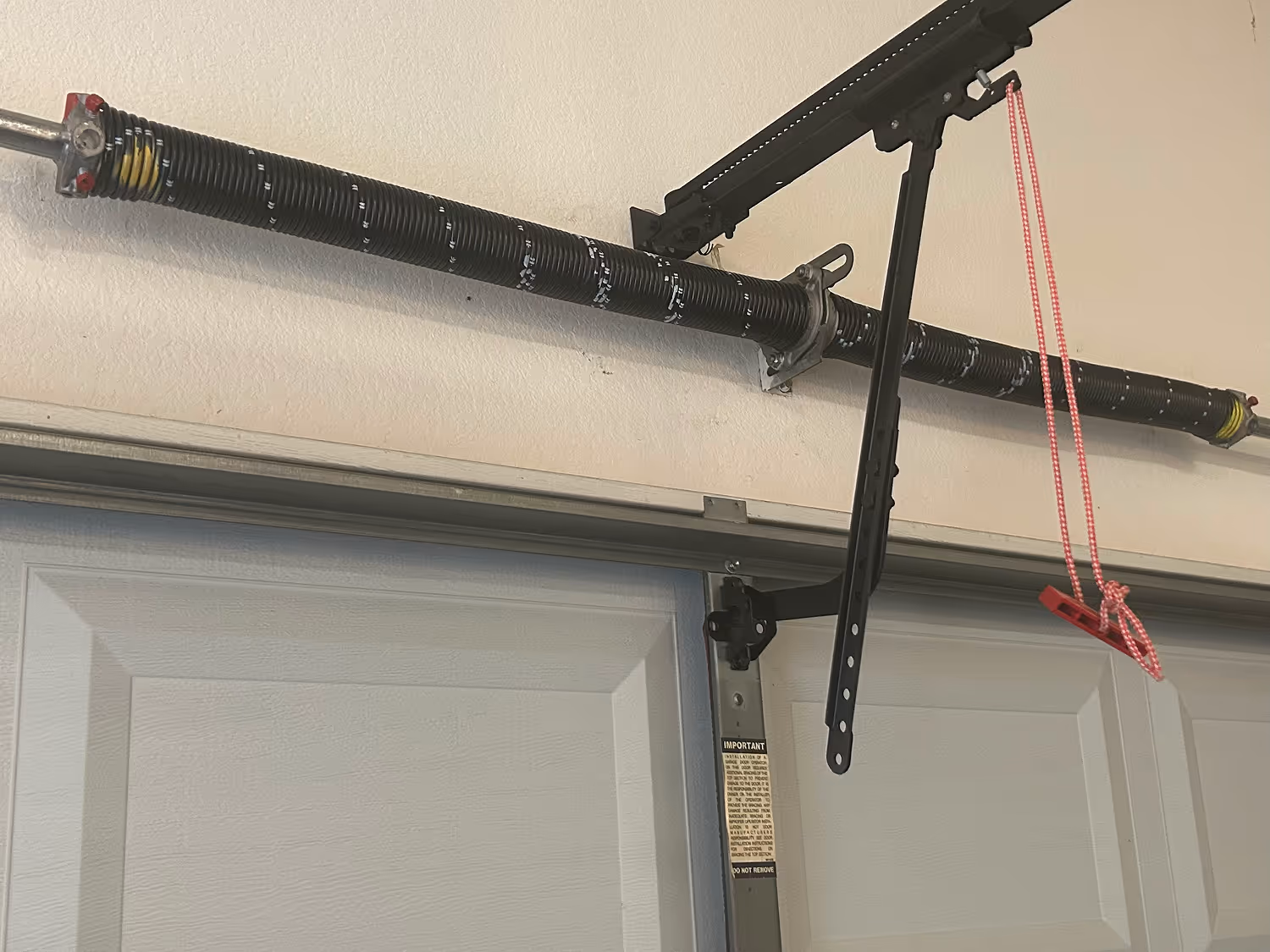 Close-up of a garage door torsion spring and metal bracket with a red release cord hanging down.
