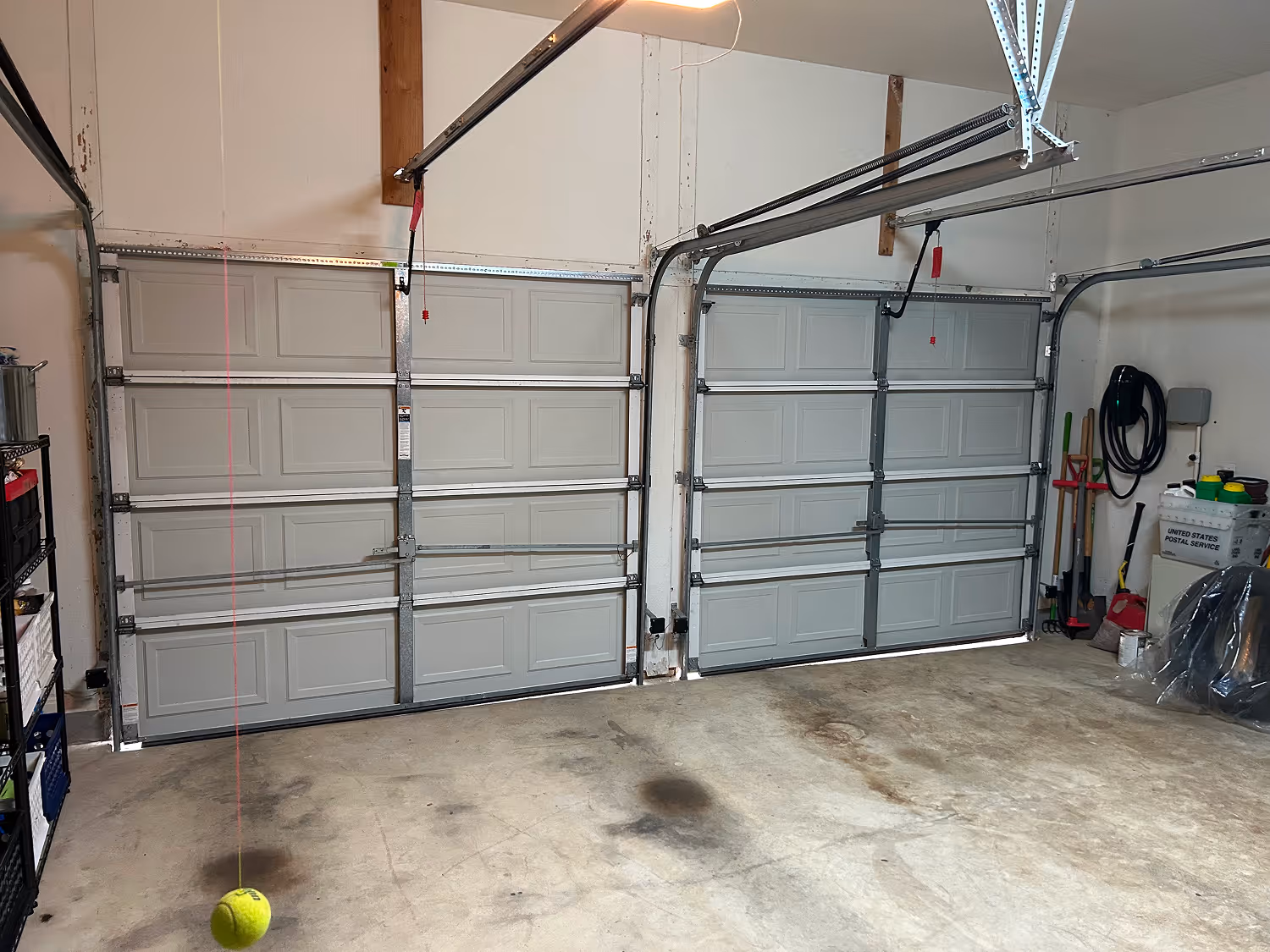 Empty garage with two closed sectional garage doors and a tennis ball hanging from a string.