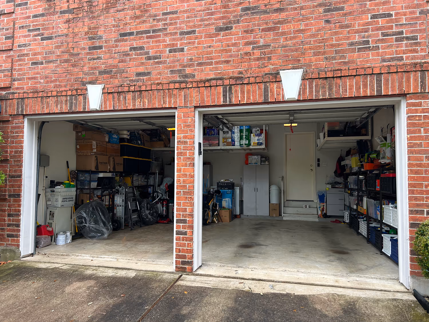 Double garage with one side cluttered with boxes and storage bins, the other side mostly clear with shelves and storage cabinets.
