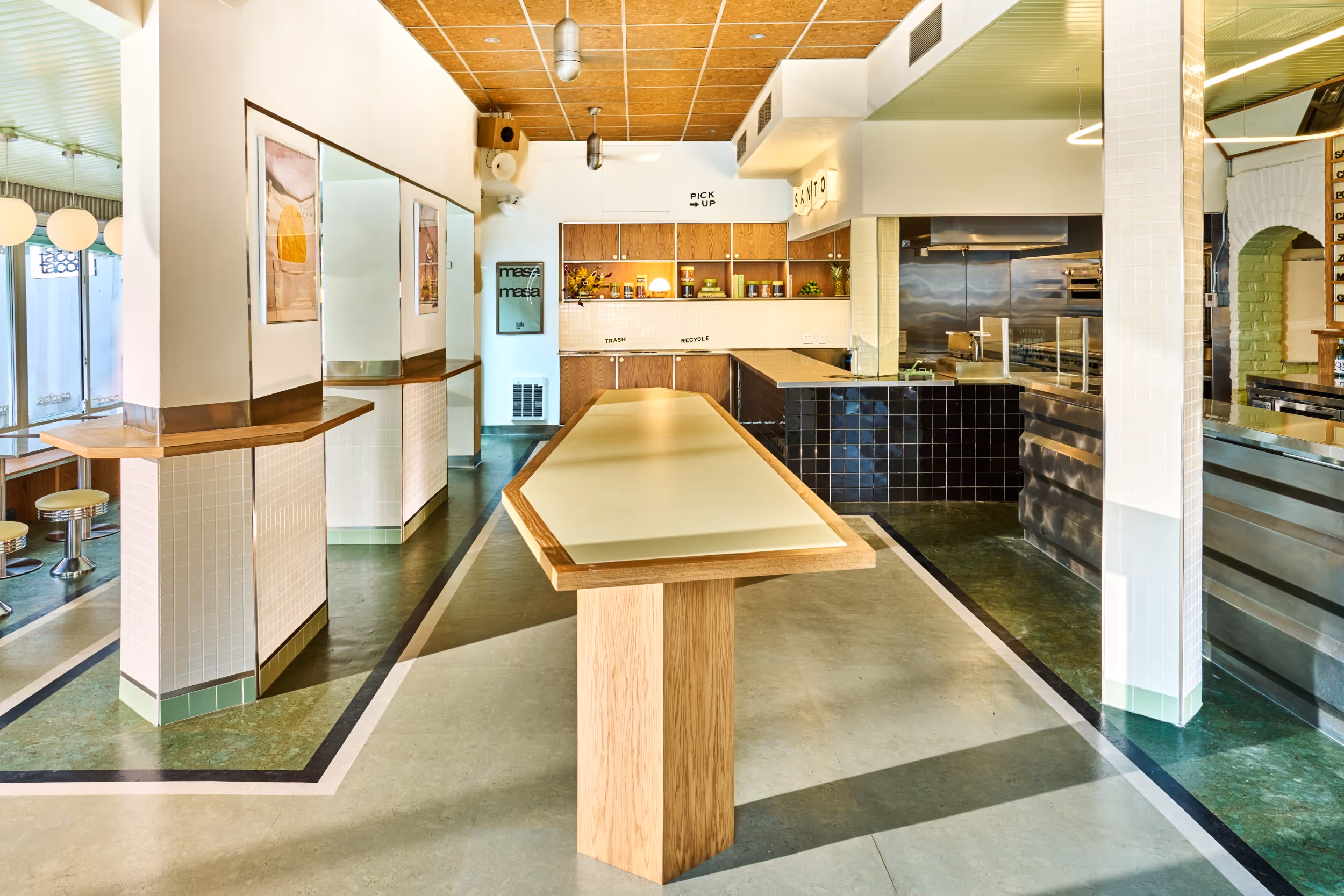 Interior of a modern, clean restaurant with tiled columns, wooden counters, and a long central table under warm lighting.