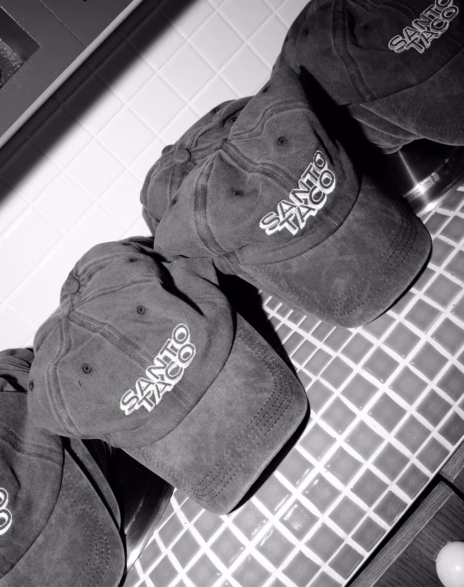Several dark-colored baseball caps with 'SANTO TACO' embroidered on the front, displayed on a tiled surface.