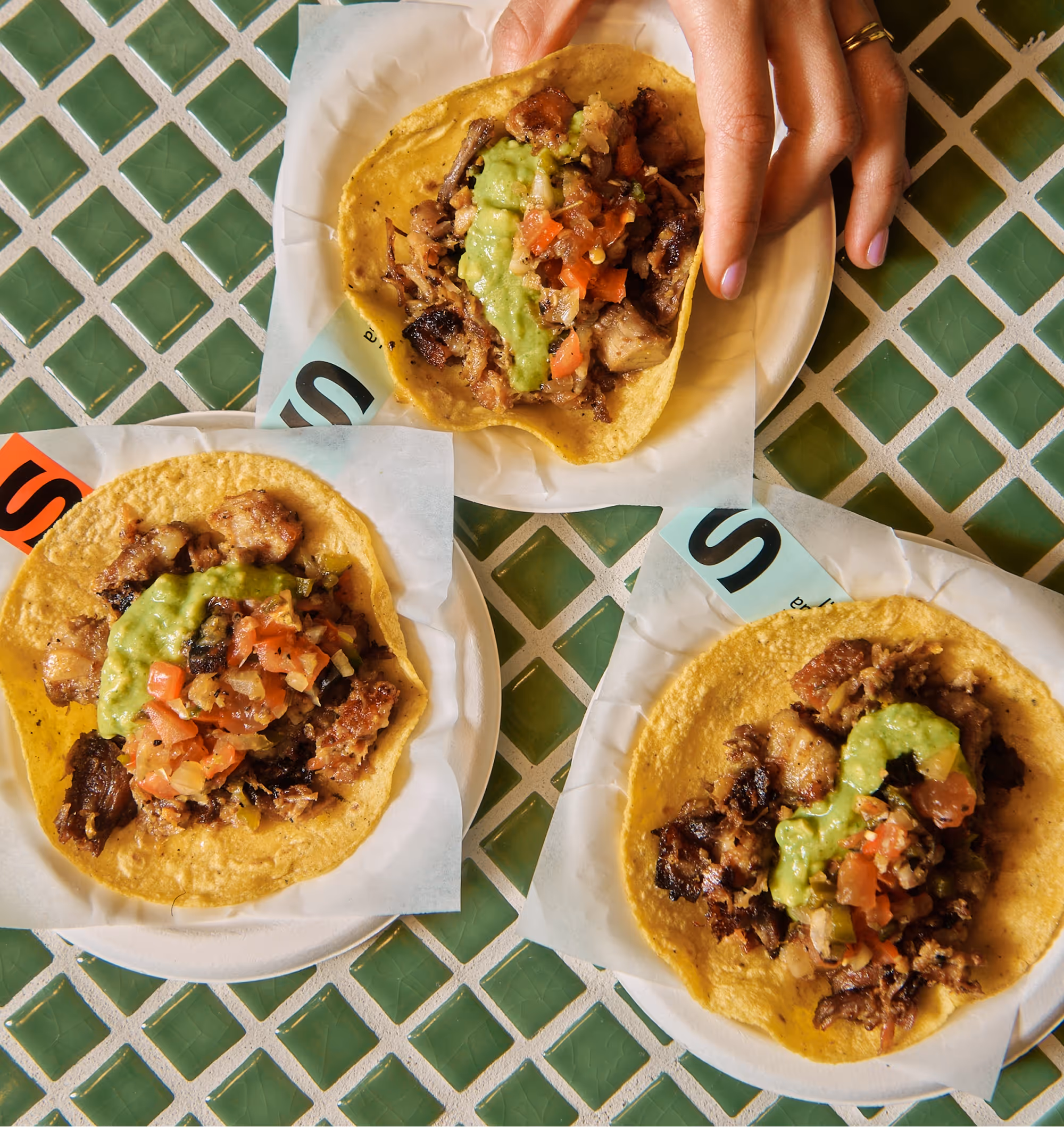 Three people grabbing their own The Pork Carnitas Taco