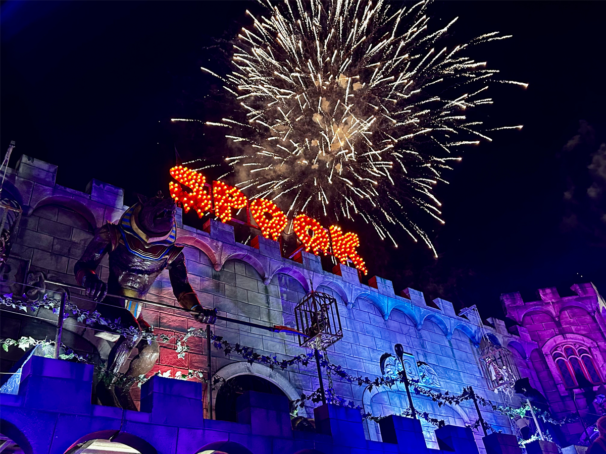 Fireworks exploding in the night sky above a castle facade decorated with a large Anubis statue and illuminated 'Spookshow' sign.
