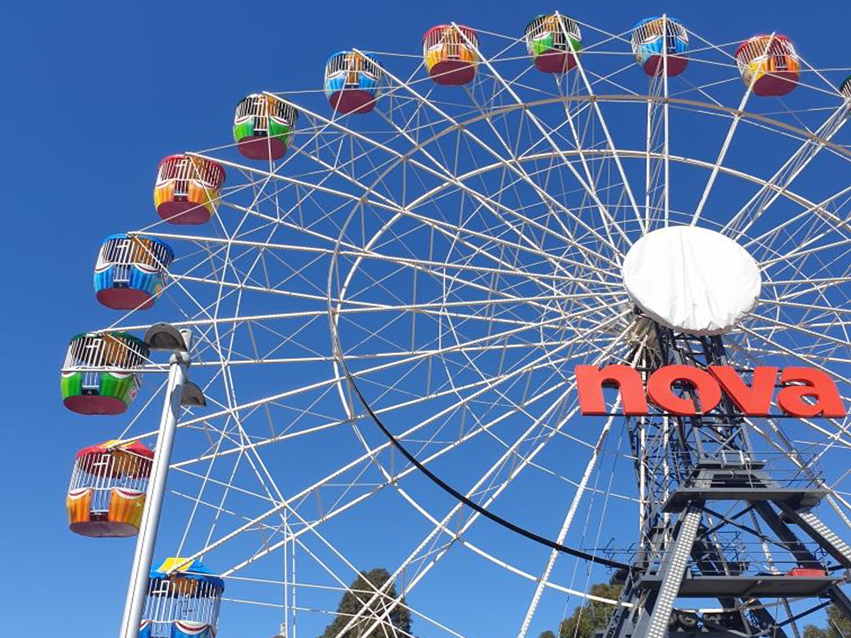 Large Ferris wheel with colorful cabins against a clear blue sky with the word 'nova' in red letters on the structure.