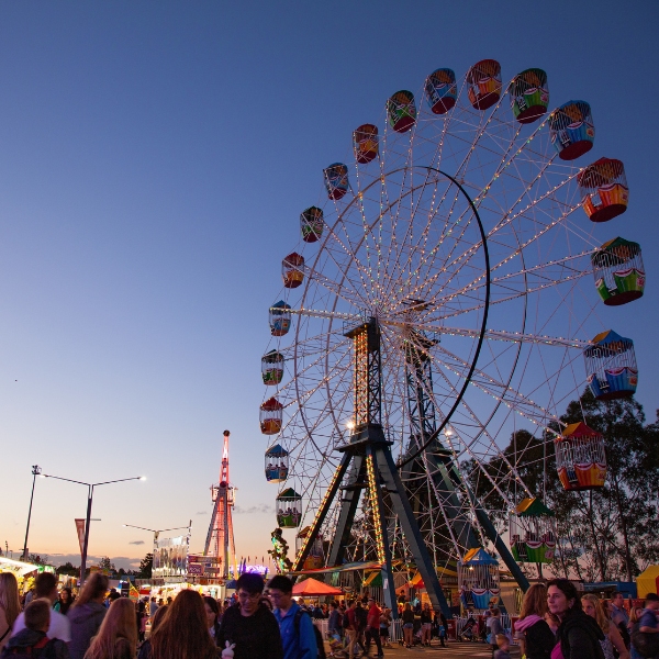 Large Ferris wheel illuminated at dusk with crowds of people at a fairground.
