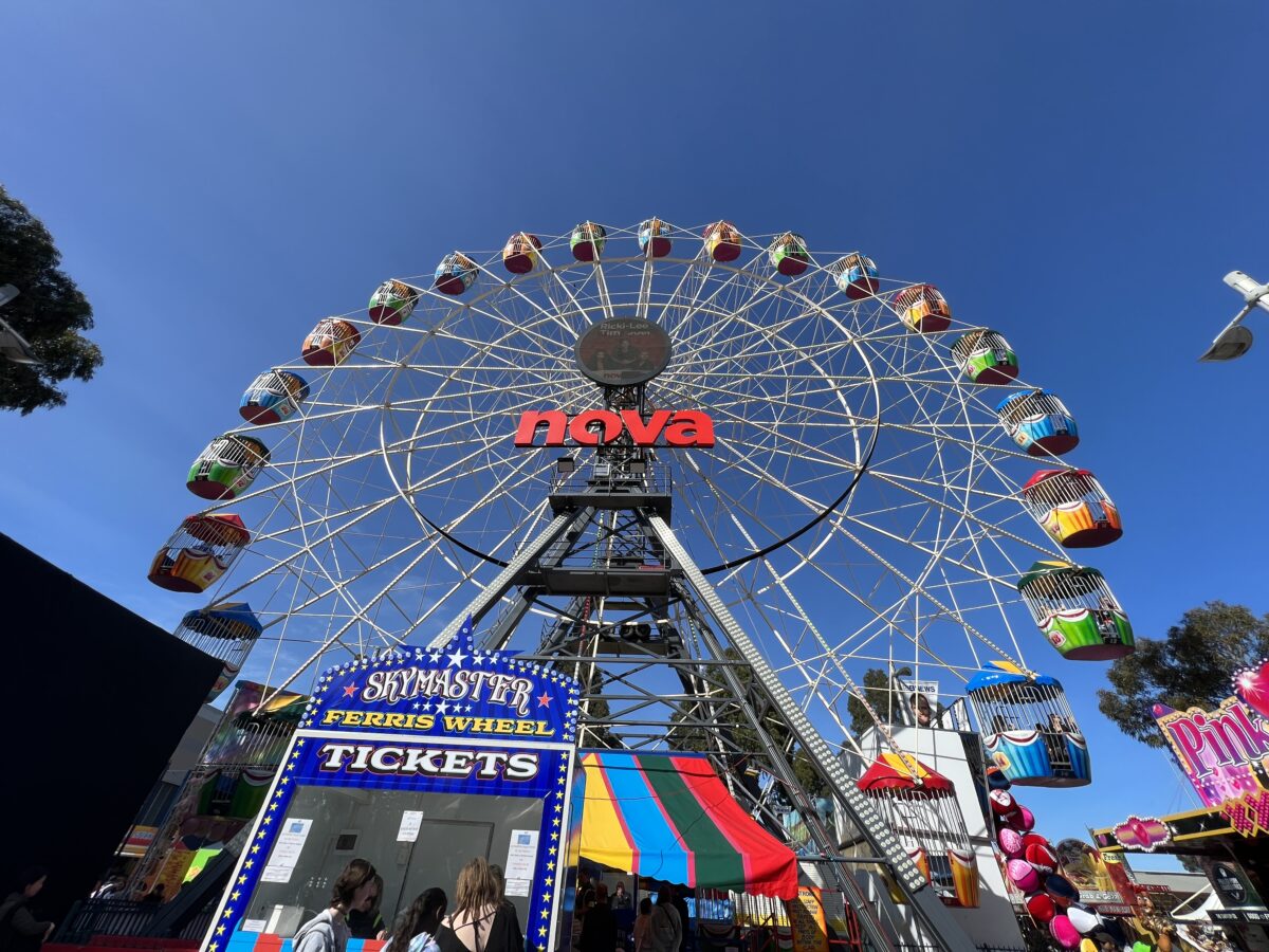 Colorful SkyMaster Ferris wheel with cabins and a ticket booth below under a clear blue sky at an amusement park.