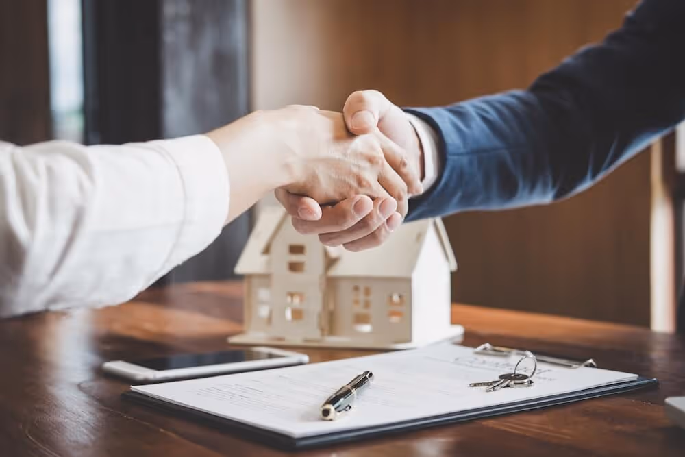 Zwei Menschen geben sich die Hand über einem Vertrag mit einem Haus im Hintergrund veranschaulicht die Qualität, die man bei Planprofi24 erhlält