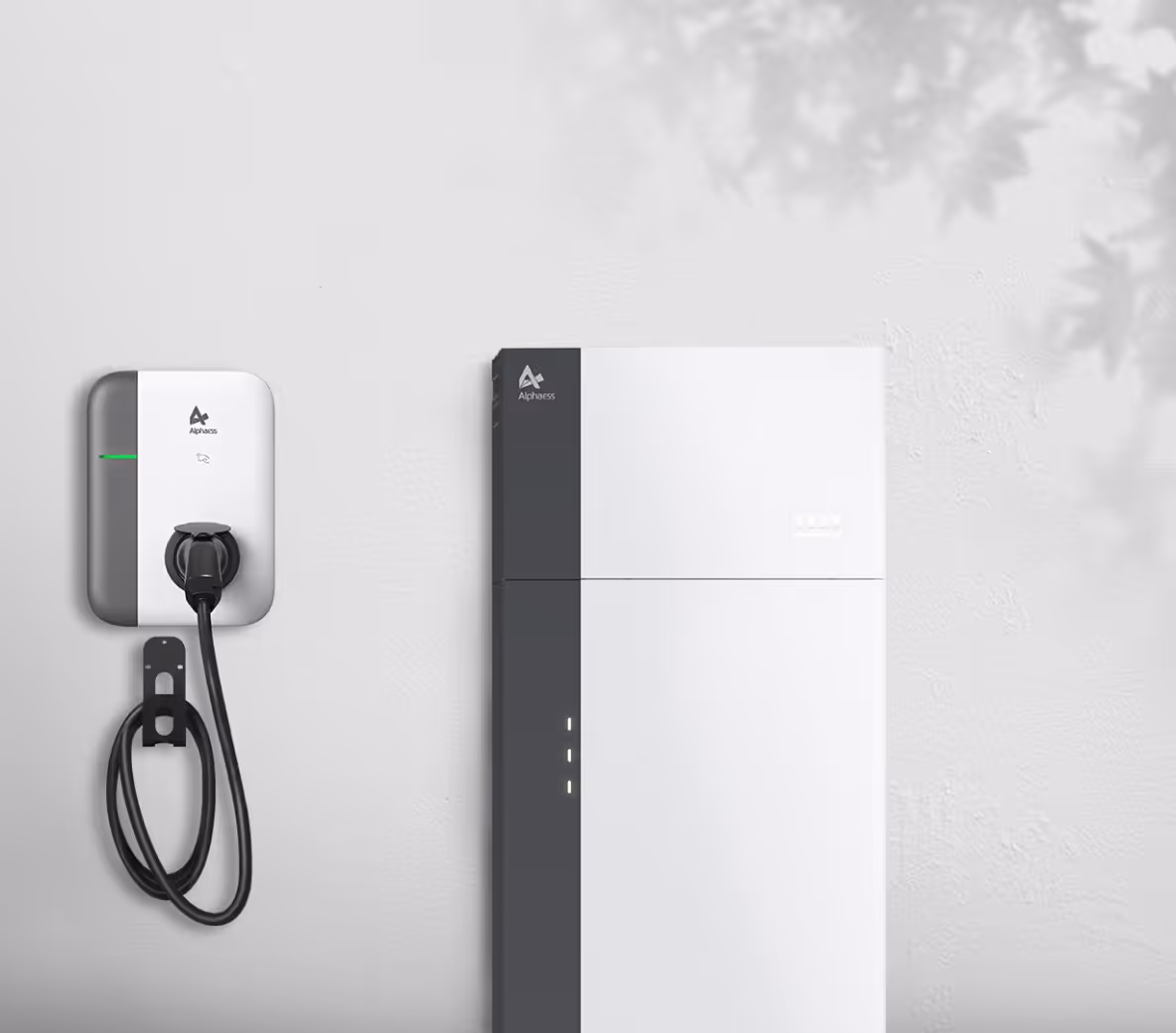 Witte thuisbatterij naast een wandgemonteerde laadunit met kabel tegen een strakke buitenmuur.