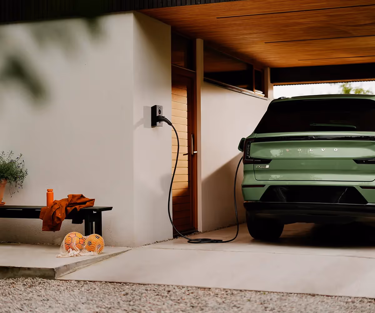Groene elektrische auto aangesloten op laadpaal naast moderne woning.