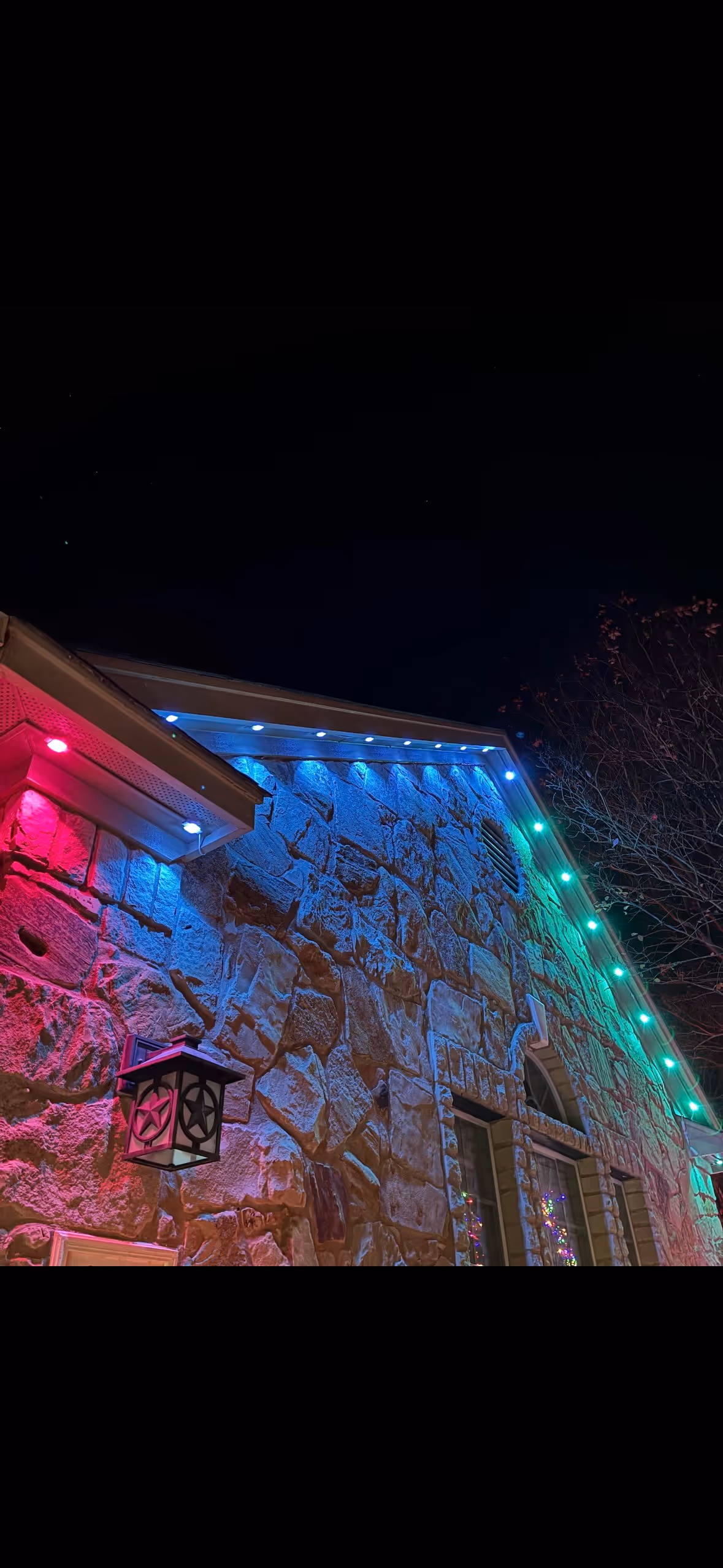 Stone house illuminated with vibrant red, blue, and green lights at night.