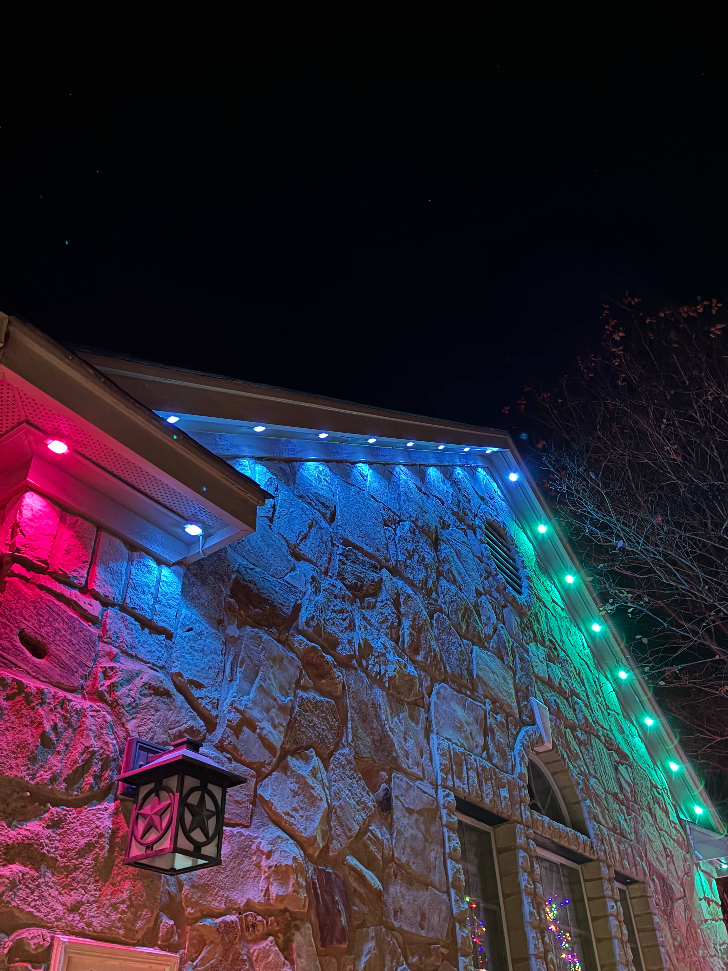 Stone house wall illuminated with red, blue, and green holiday lights at night.