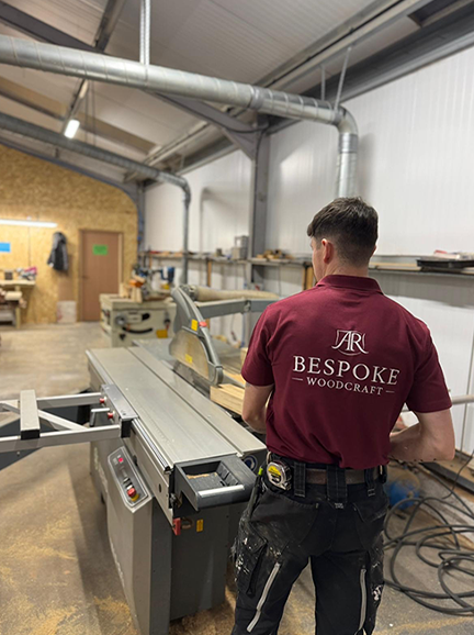 Man in red Bespoke Woodcraft shirt working with wood on a table saw in a workshop.