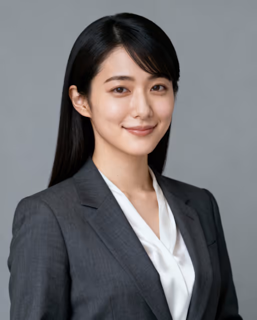 Confident woman with long black hair wearing a dark gray suit and white blouse against a plain gray background.