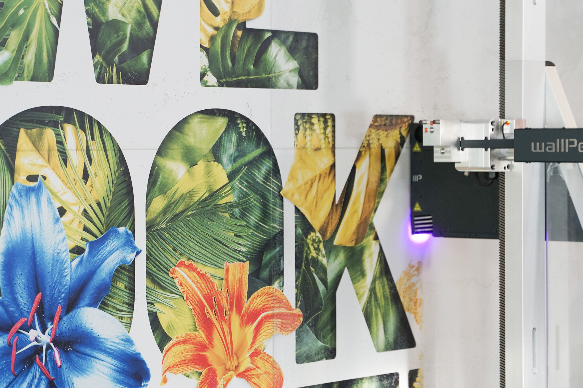 Nahaufnahme eines Druckers, der einen farbenfrohen Blumen- und Blattmusterdruck auf eine weiße Fläche mit Buchstaben anfertigt.