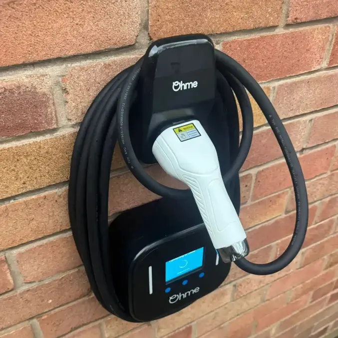 Ohme Home Pro EV charger installed on a brick wall with white tethered charging connector