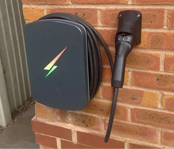 Black home EV charger with cable neatly coiled on an exterior brick wall