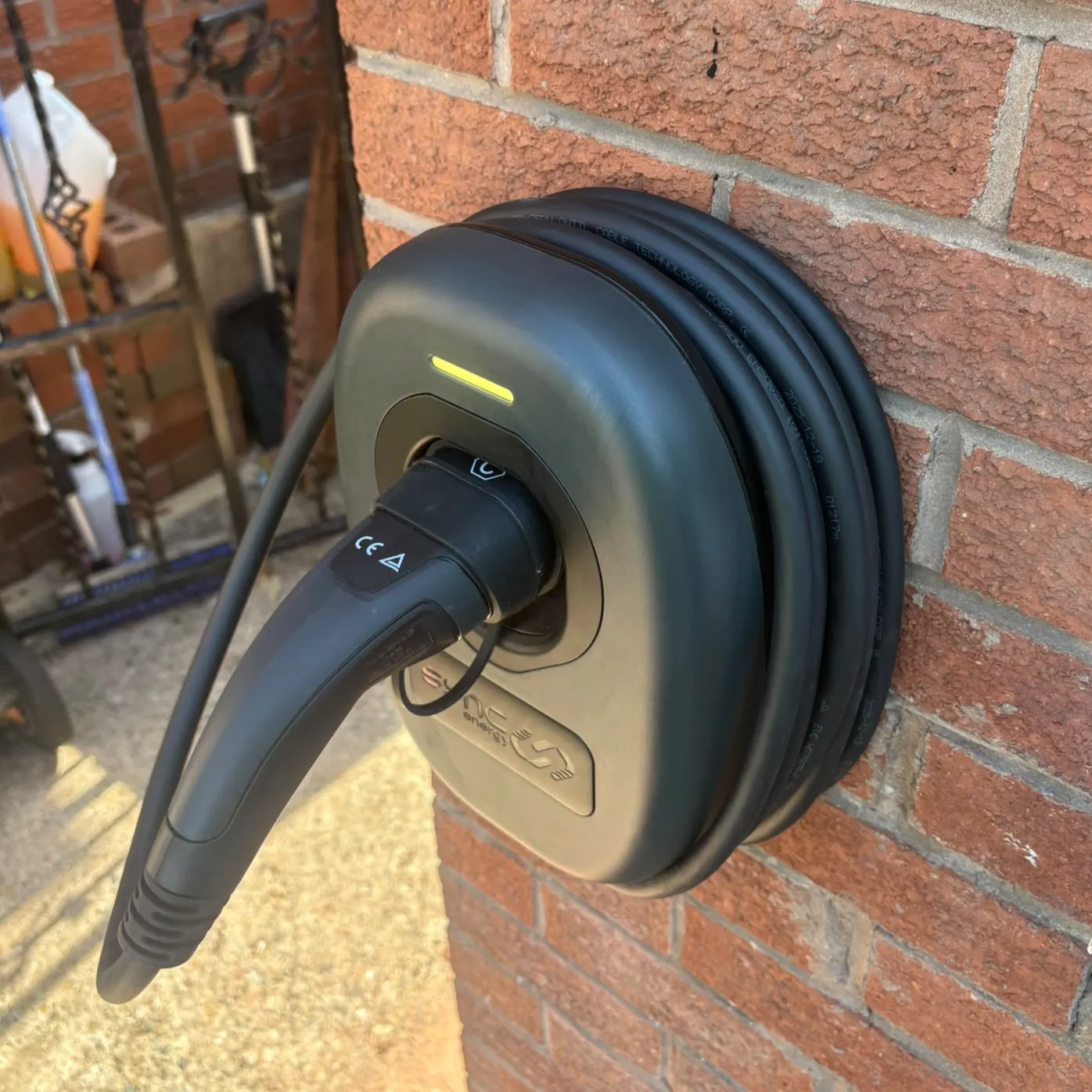 Sync EV charger installed on a brick exterior wall with cable wrapped around the unit