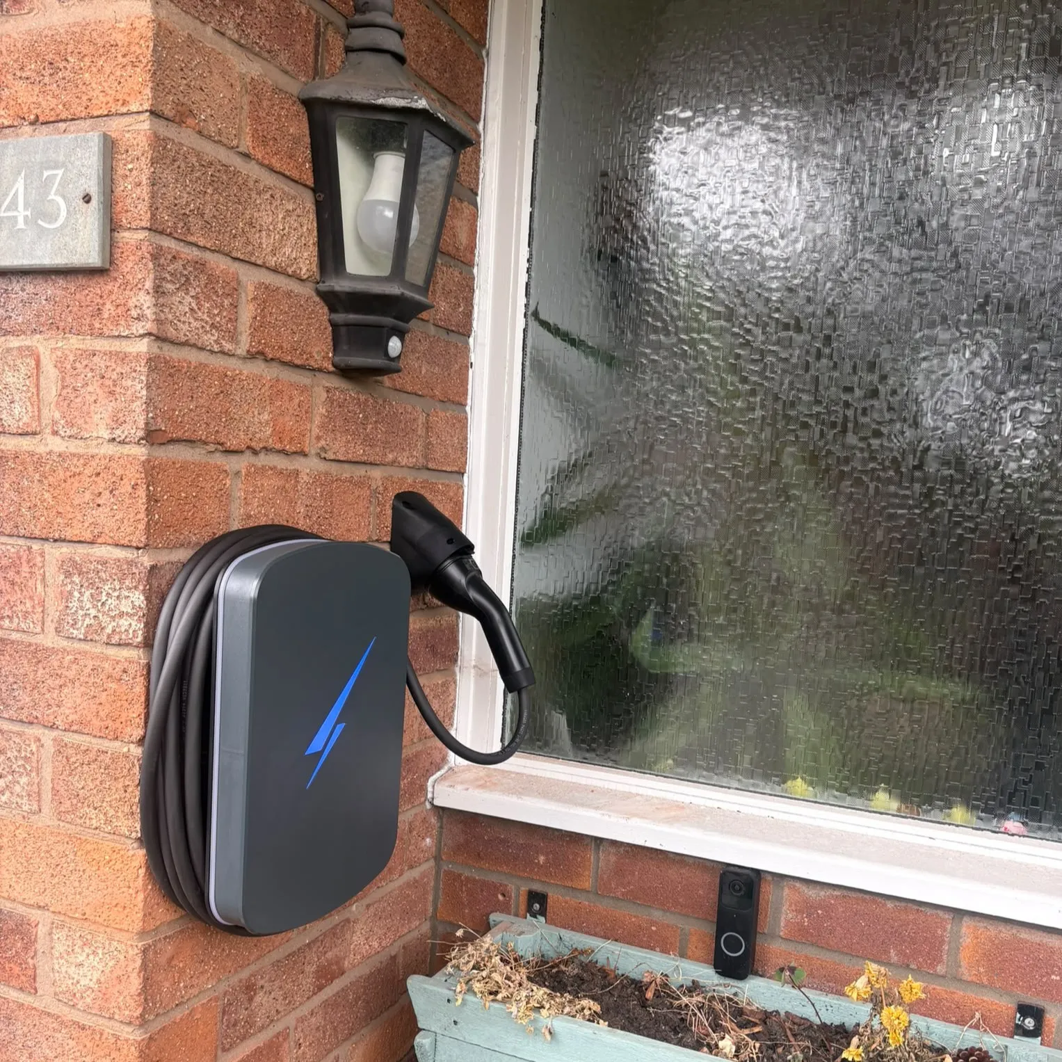 Dark Hypervolt EV charger mounted on a brick wall beneath an outdoor light beside a window