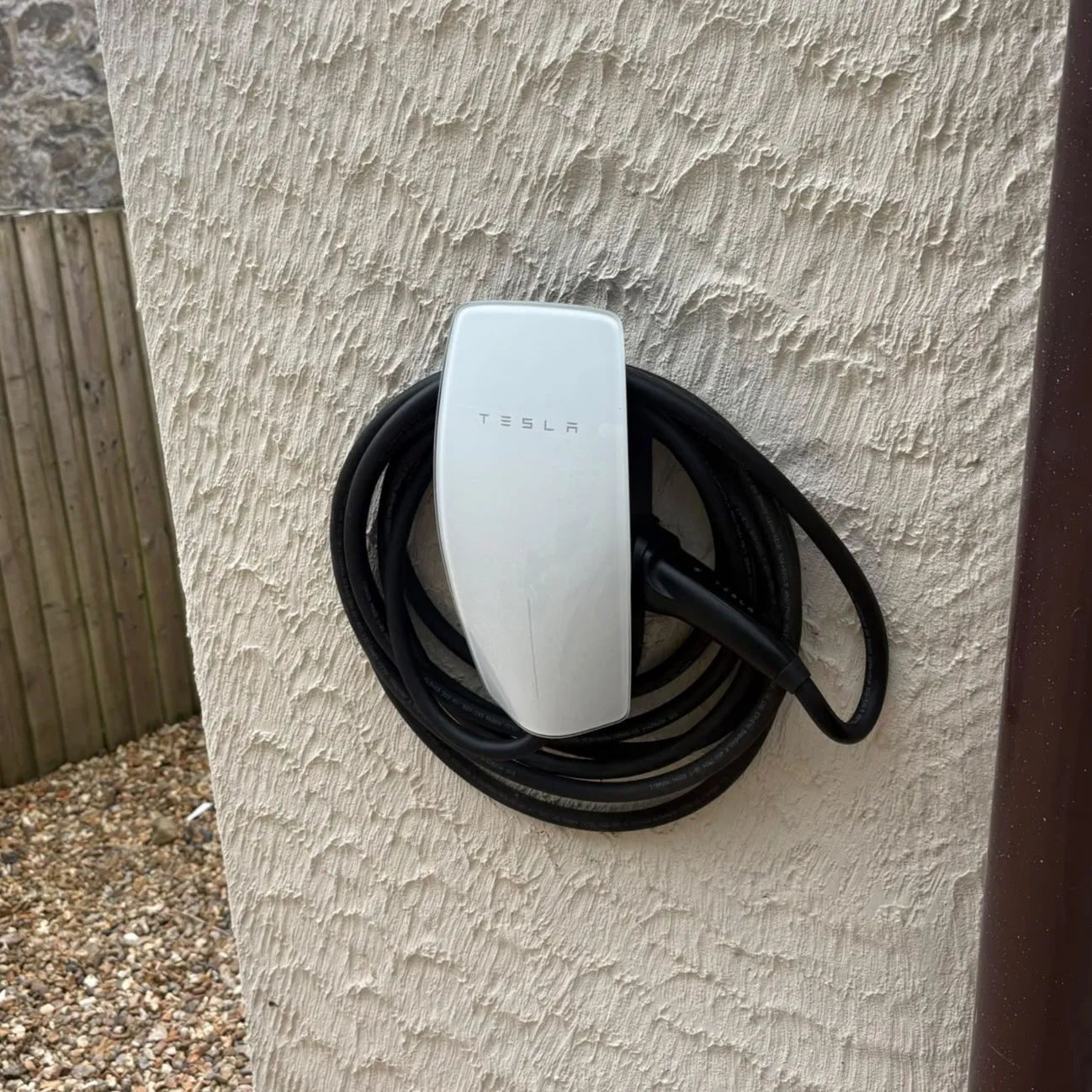 White Tesla Wall Connector installed on a rendered exterior wall with coiled charging cable
